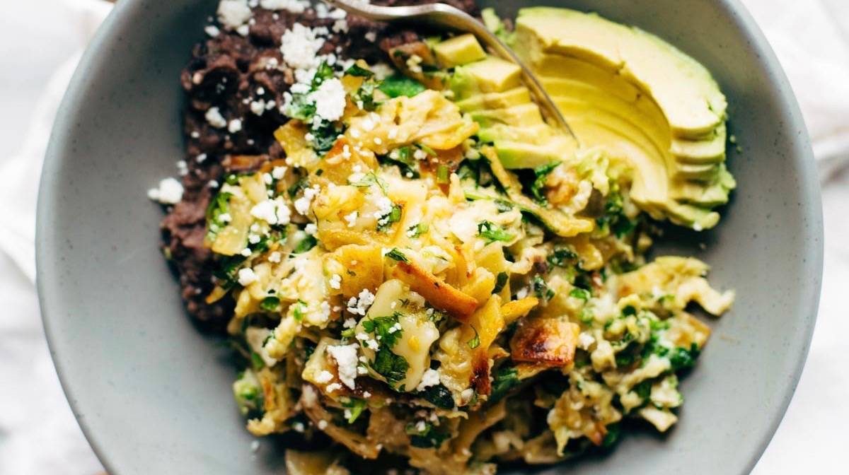 Migas in a bowl with avocado and refried black beans.
