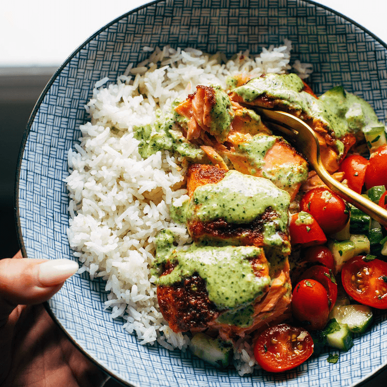 Salmon with basil sauce in a bowl with rice and tomato salad.