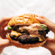 Hands holding a juicy smash burger with sauce.